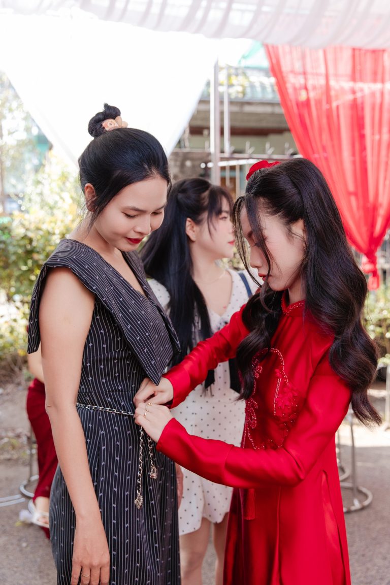 Cô dâu mặc áo dài đỏ cúi xuống cài lại dây áo cho một người khách trong ngày cưới