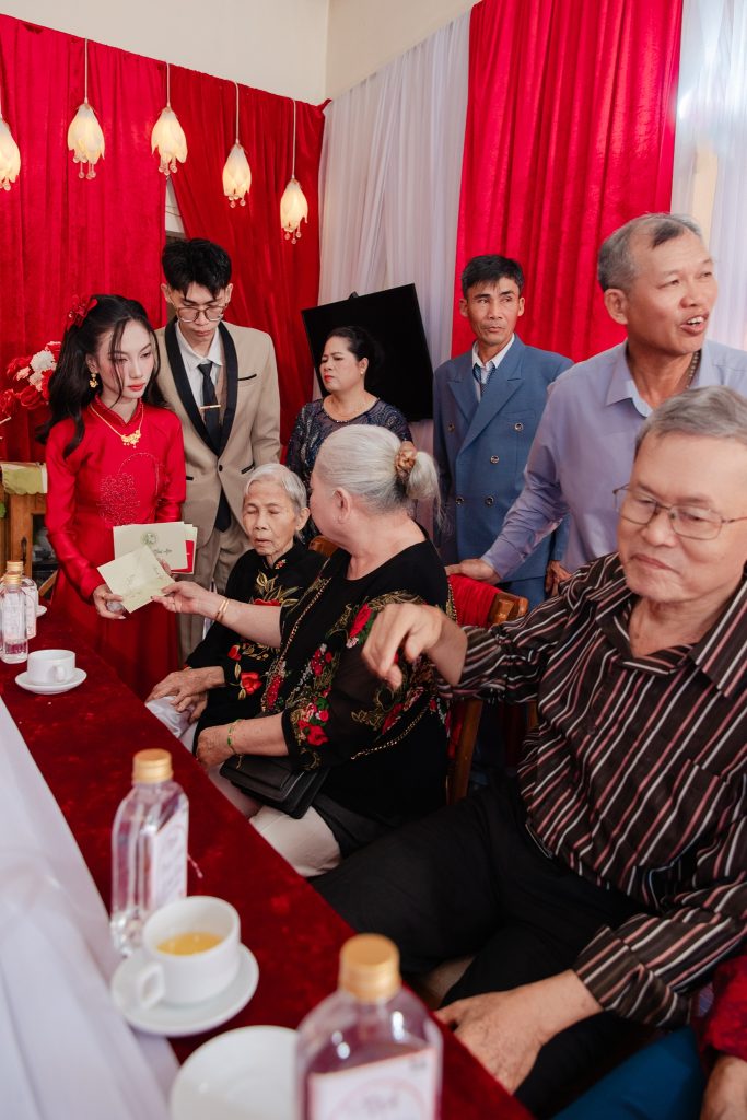 Hai cụ ngồi trao phong bì cho cô dâu ở bàn gia tiên, cả nhà đứng phía sau